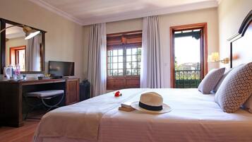 Una habitación de hotel con cama, escritorio, televisor y ventana con cortinas.