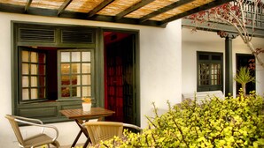 A traditional building with a covered patio, two windows with green shutters, and a table with chairs. - Hotel Rural Finca de la Florida (San Bartolome)