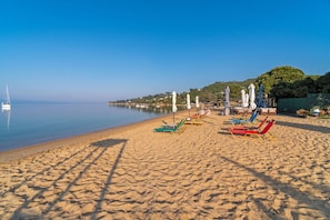 Una spiaggia con file di lettini e ombrelloni, un mare calmo e un cielo sereno.