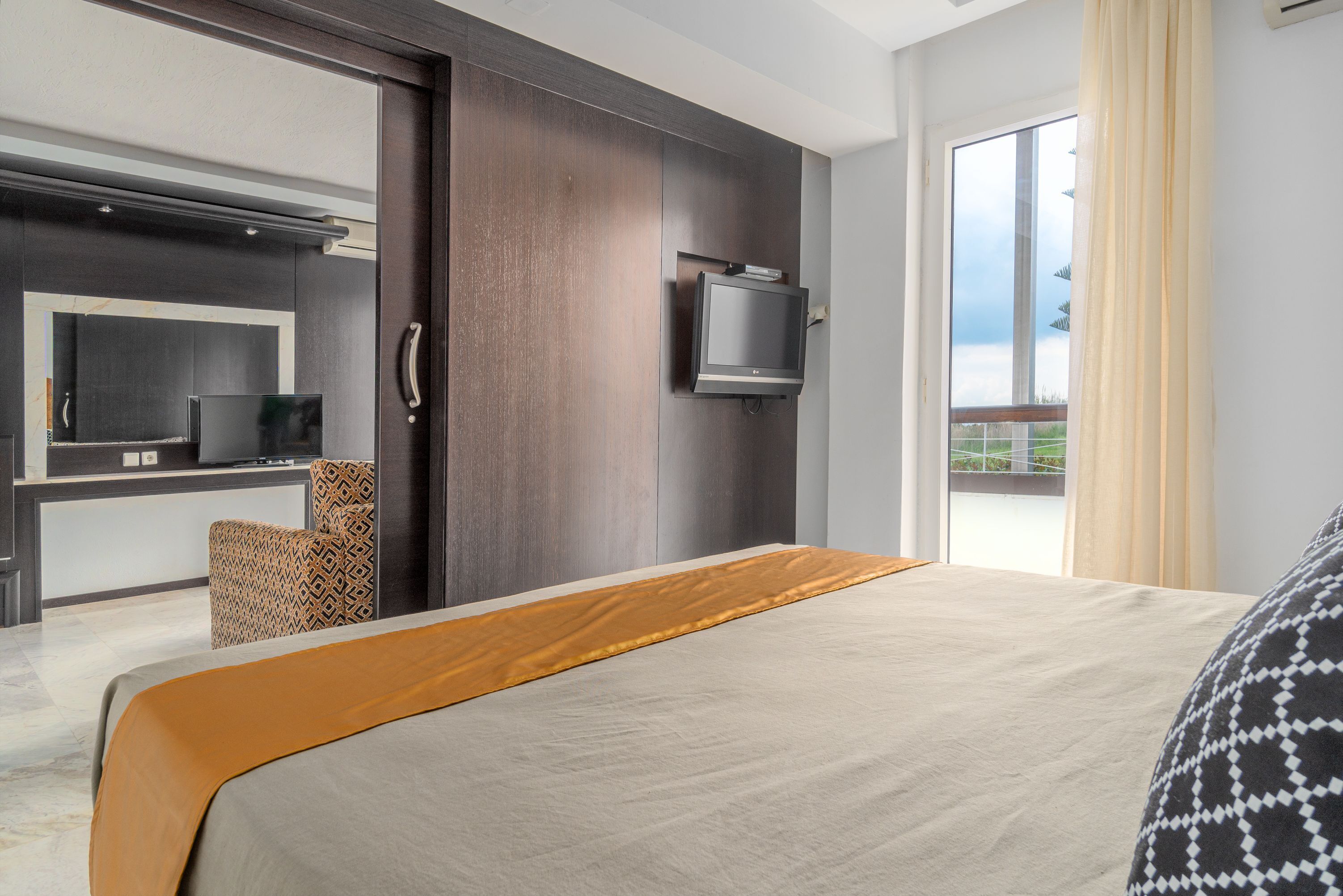 Una habitación de hotel moderna con una cama grande, un televisor de pantalla plana montado en la pared, un sofá y un balcón con vistas.