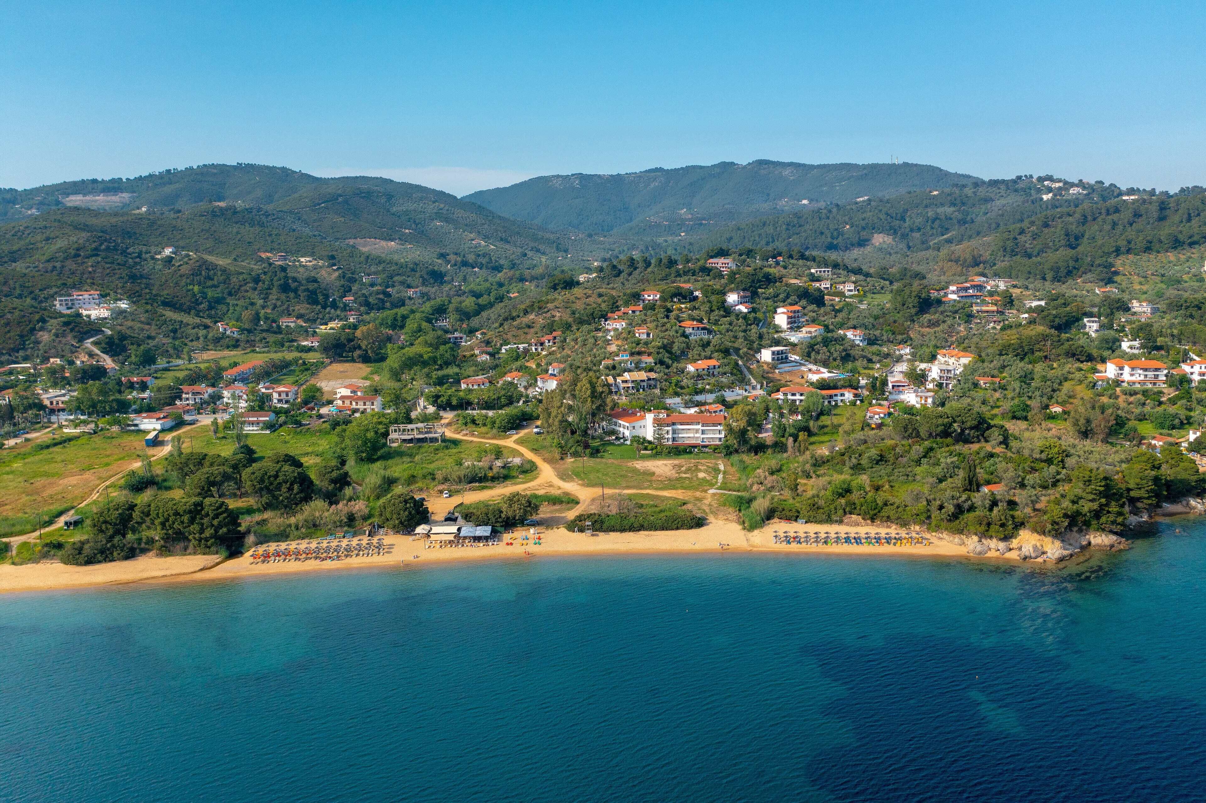 A coastal town with houses, a beach, and a mountainous backdrop.