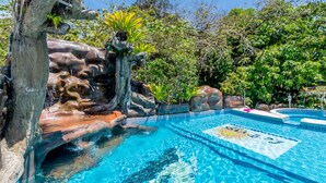 Une piscine agrémentée d’une cascade, entourée d’une végétation luxuriante et surplombée d’un ciel bleu azur.