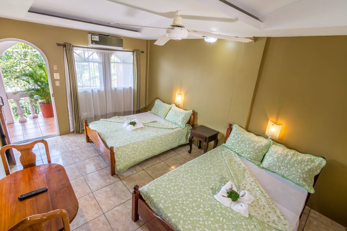 Une chambre d’hôtel avec deux lits, une table à manger, des chaises, une petite table et un ventilateur de plafond.