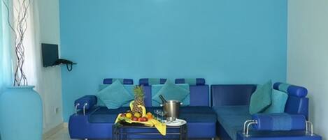 A living room with a blue sofa, a coffee table with fruits and a book, and a large vase.