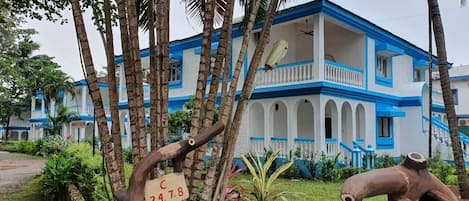 A building with a blue and white facade, surrounded by palm trees and greenery.