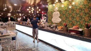 A restaurant with a long counter, decorative wall, and hanging lights. - Paradise Village Beach Resort (Calangute)