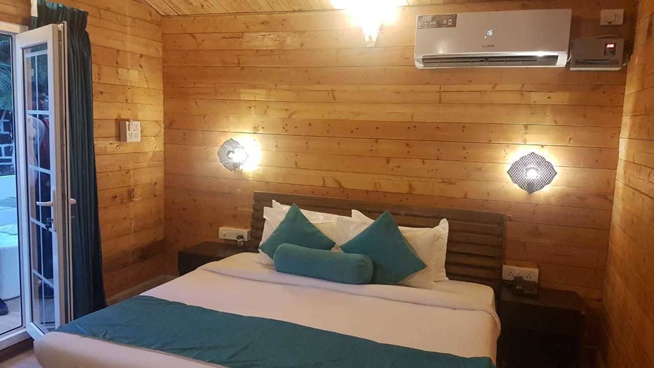 Une pièce aux murs lambrissés, comprenant un lit, deux lampes fixées au mur, un appareil de climatisation et une porte-fenêtre coulissante.