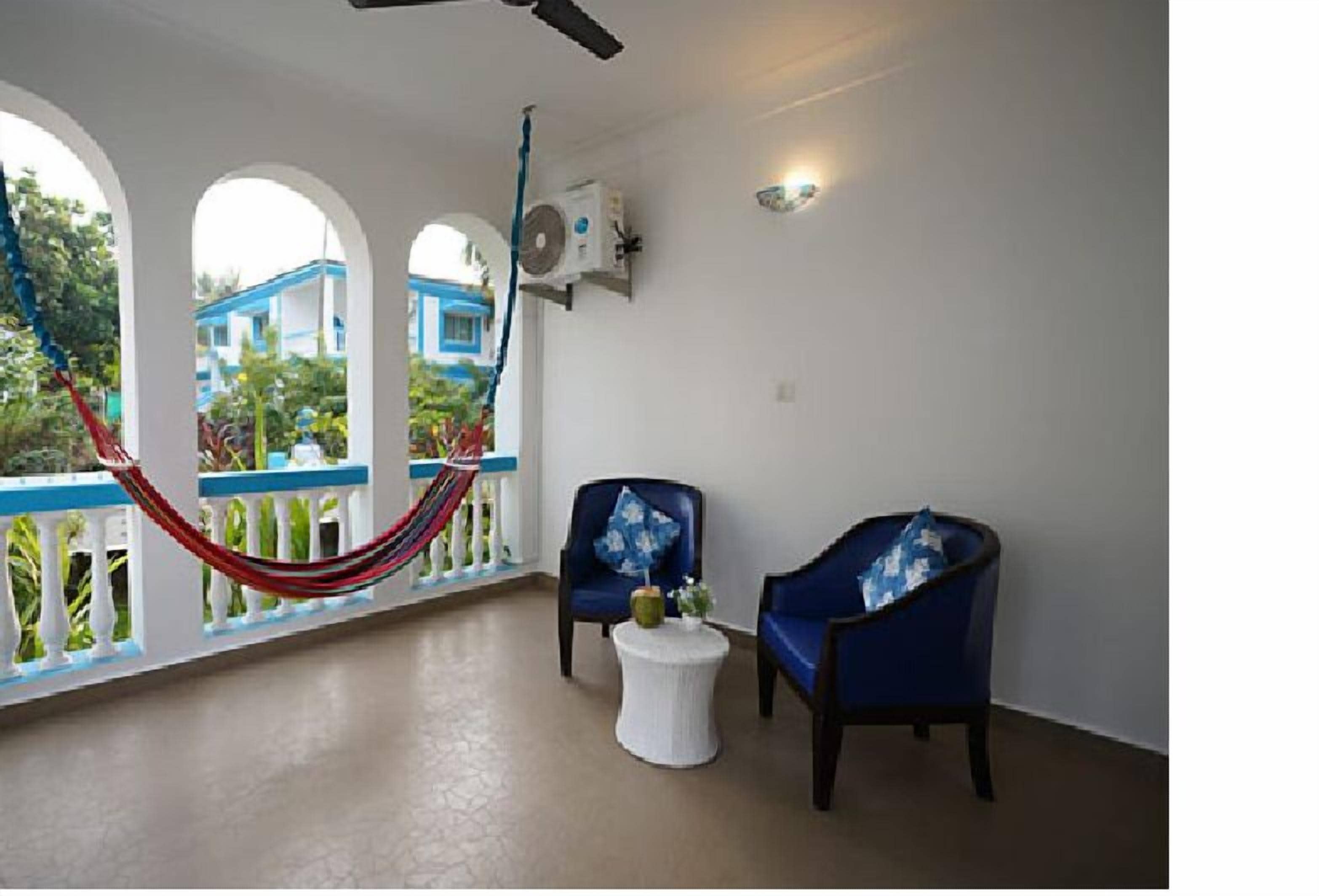 A room with a hammock, two blue armchairs, a small white table, and a ceiling fan.