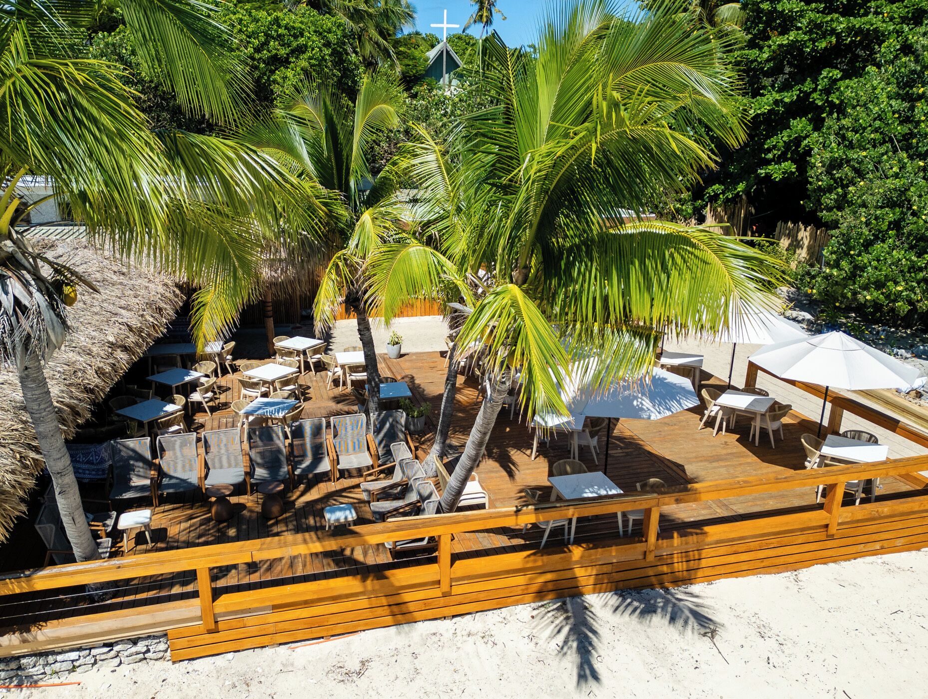 Una terraza de madera con mobiliario exterior y palmeras.
