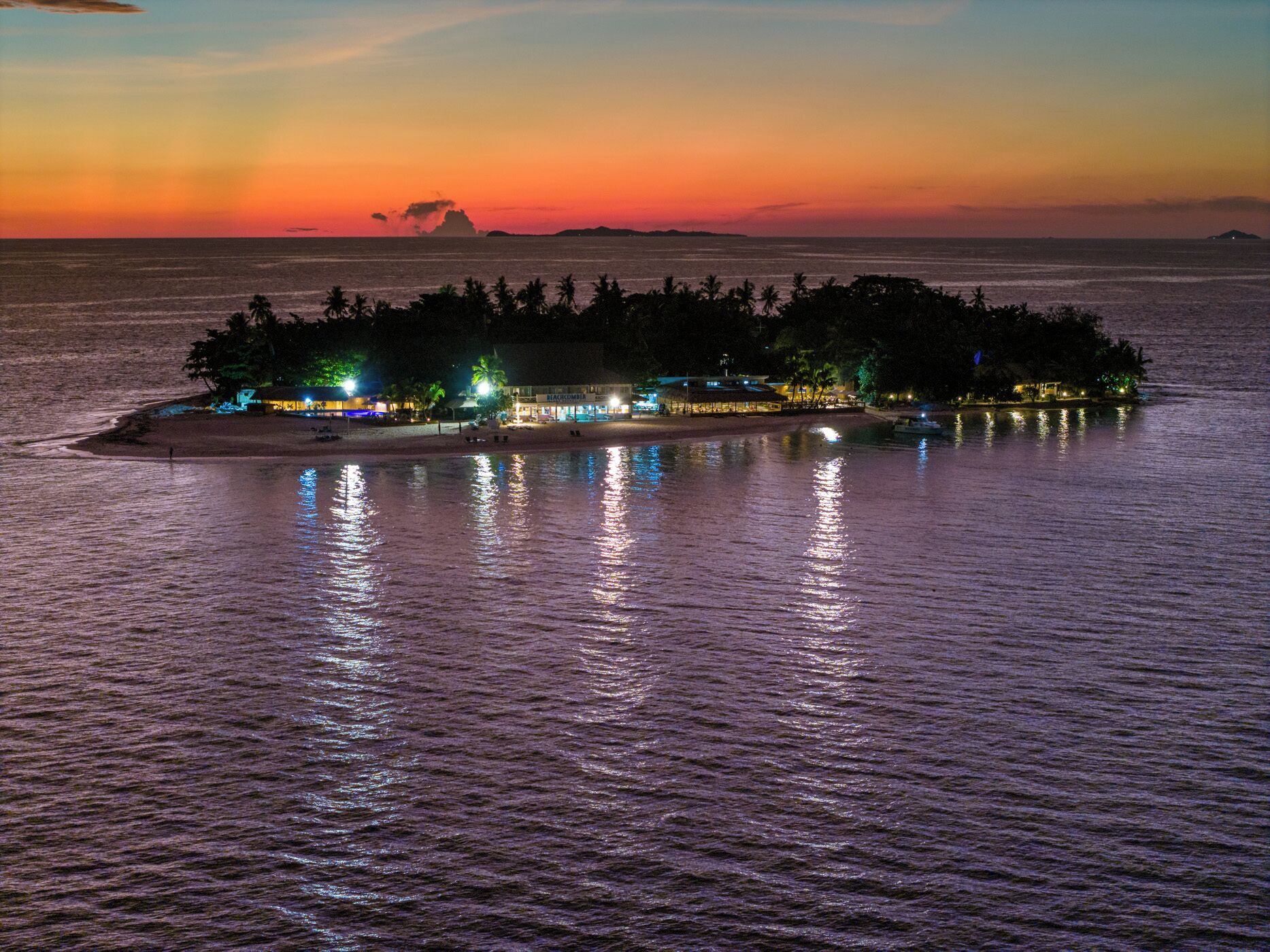 A tropical island resort with beachfront accommodations, palm trees, and a sunset view.
