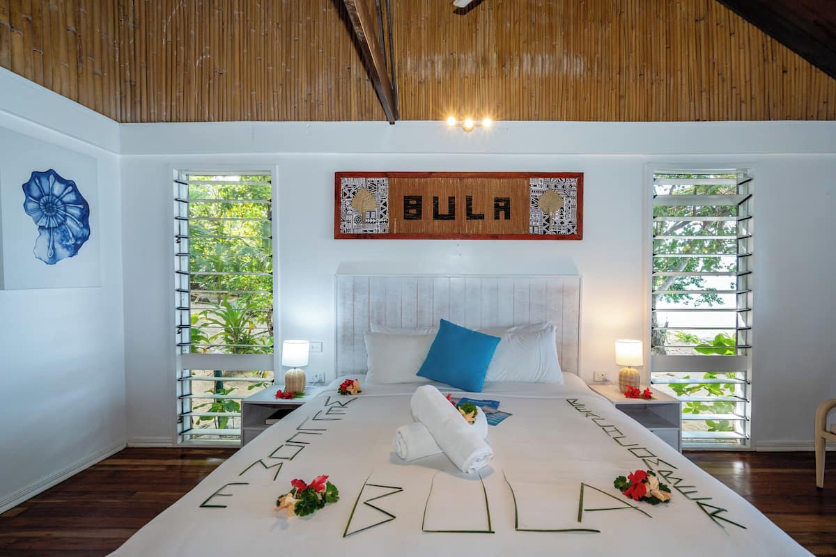 Une chambre bien éclairée, avec un grand lit, deux tables de chevet et un plafond en bois.