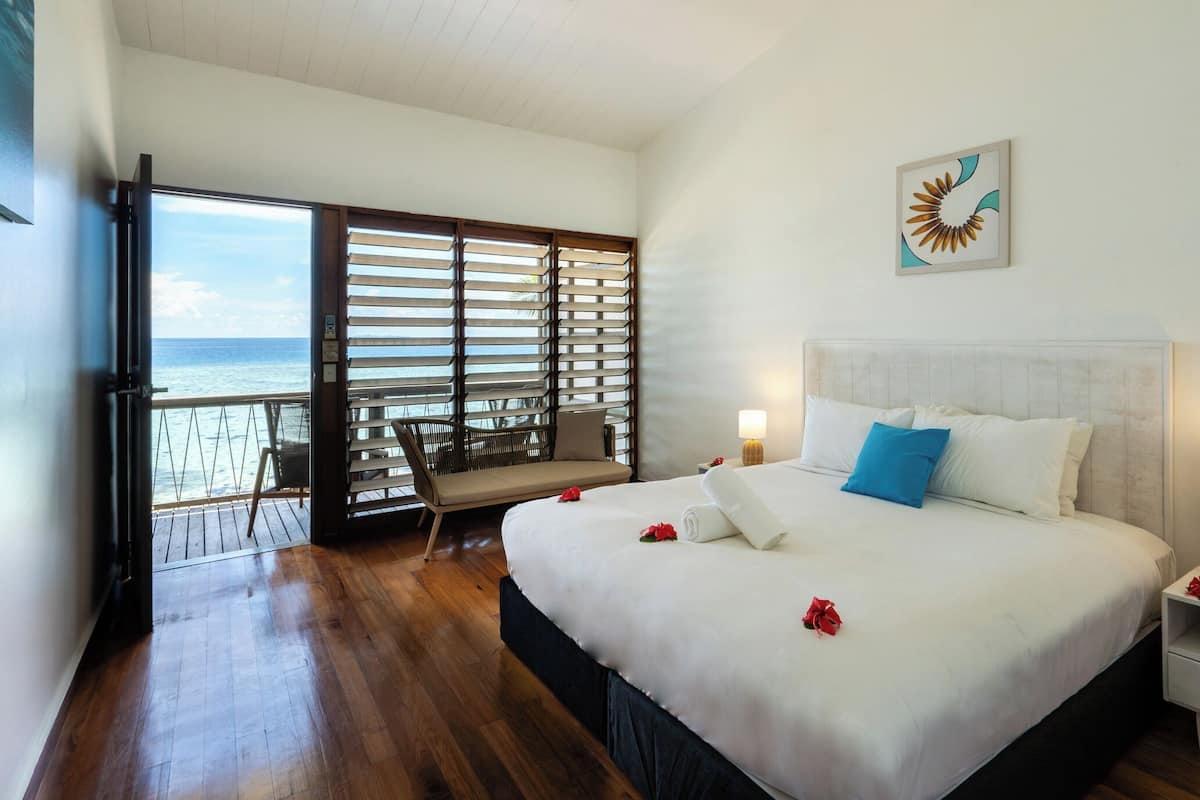Une chambre d’hôtel avec un grand lit, une table de chevet, une chaise et un balcon donnant sur l’océan.