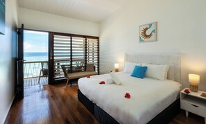 A hotel room with a large bed, a nightstand, a chair, and a balcony with a view of the ocean.