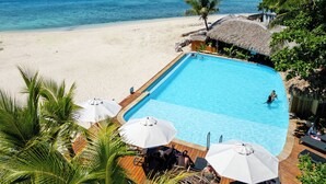 A poolside view with a clear view of the ocean, a thatched-roof structure, and a wooden deck with umbrellas. - Beachcomber Island Resort (Beachcomber Island)
