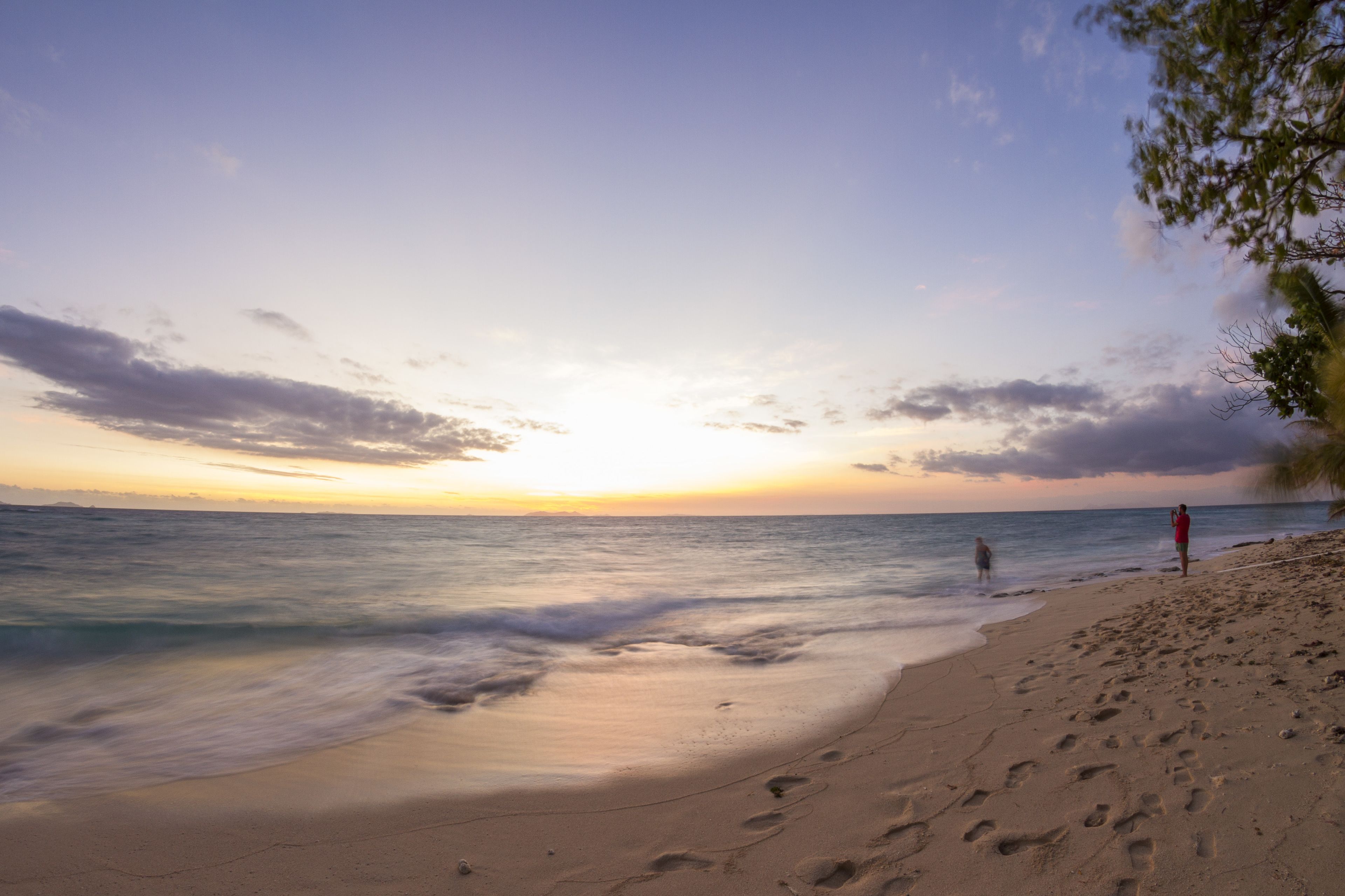 A beach with footprints, a person in a red shirt, and another person in the water.