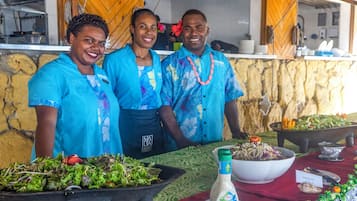 Tres personas de pie frente a una mesa de buffet con diversos platos.