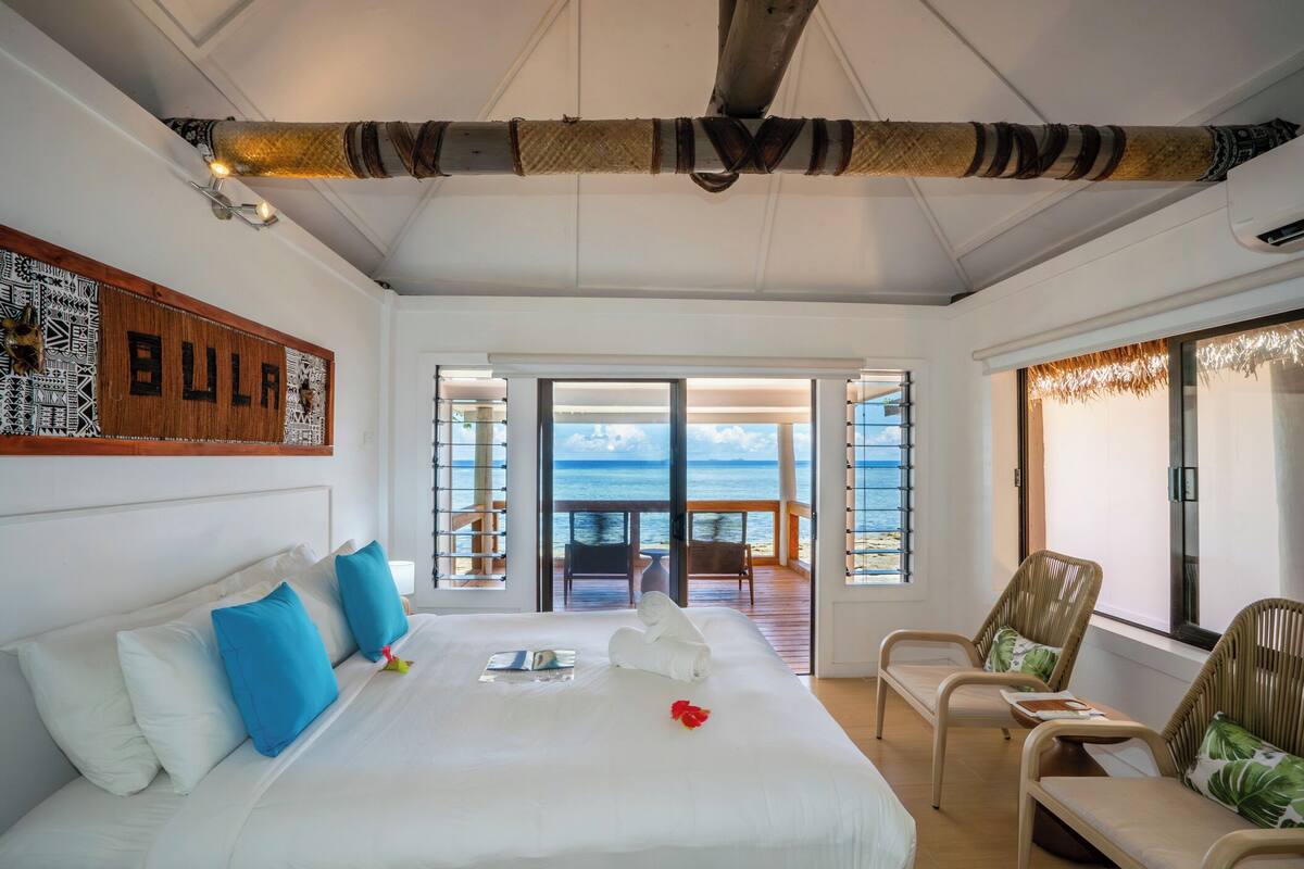 Une chambre avec un grand lit, une vue sur la mer et un balcon équipé de chaises.