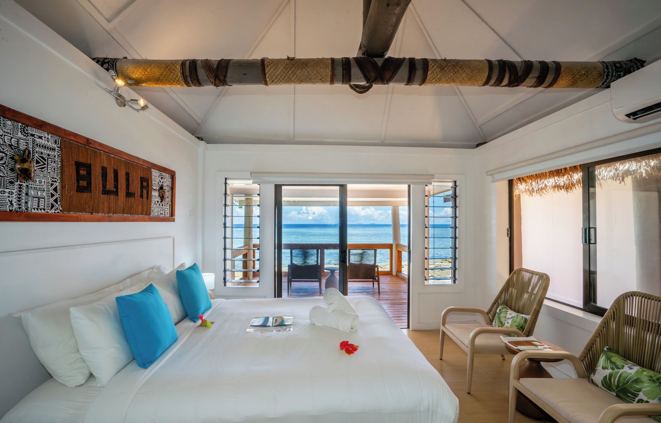 A bedroom with a large bed, a view of the sea, and a balcony with chairs.