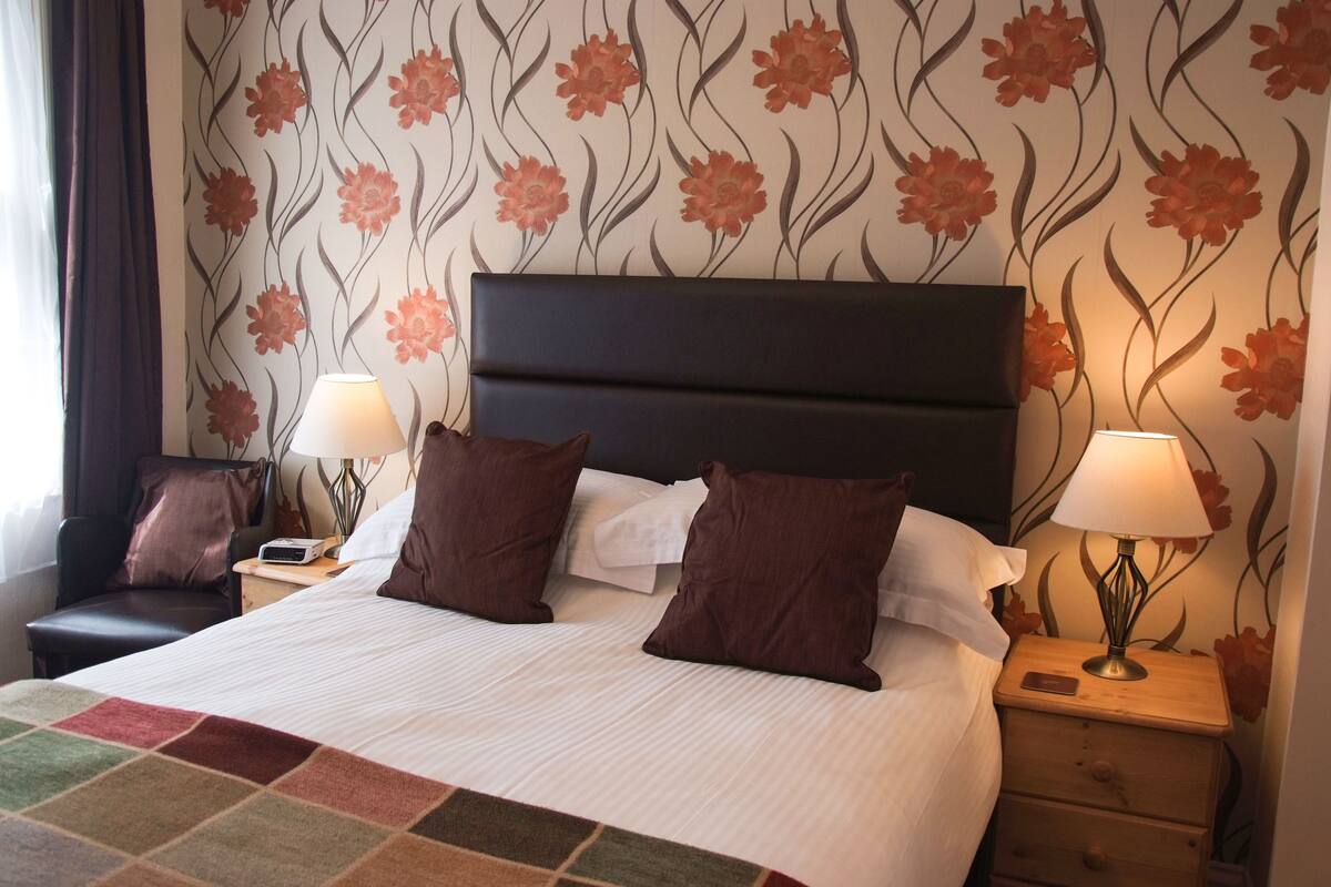 A hotel room with a large bed, two bedside tables, a chair, and floral wallpaper.