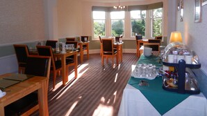 A dining area with wooden tables and chairs, a buffet setup, and large windows allowing natural light. - Overcombe House (Yelverton)