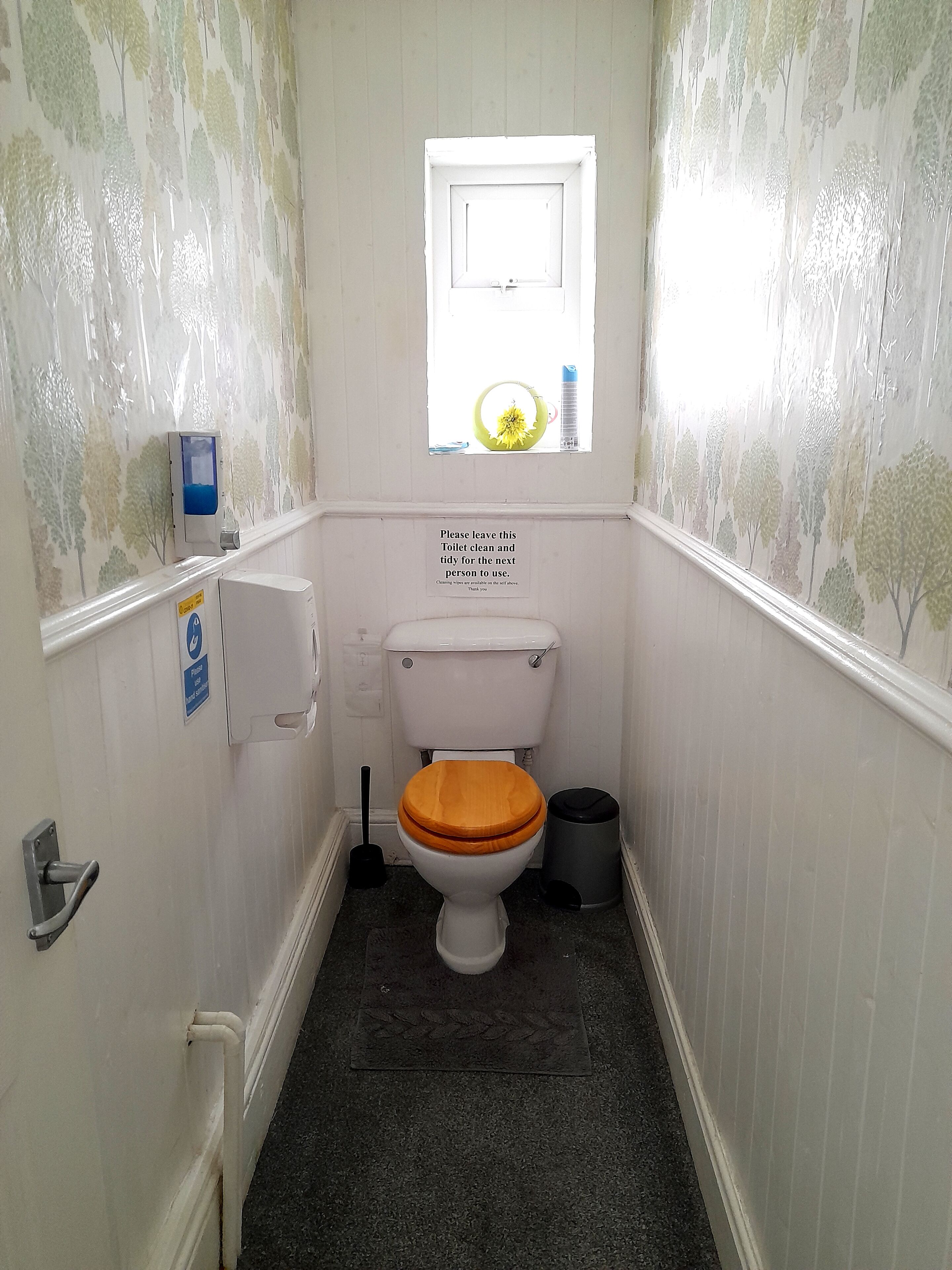 A small, narrow bathroom with a toilet, a hand dryer, and a trash can.