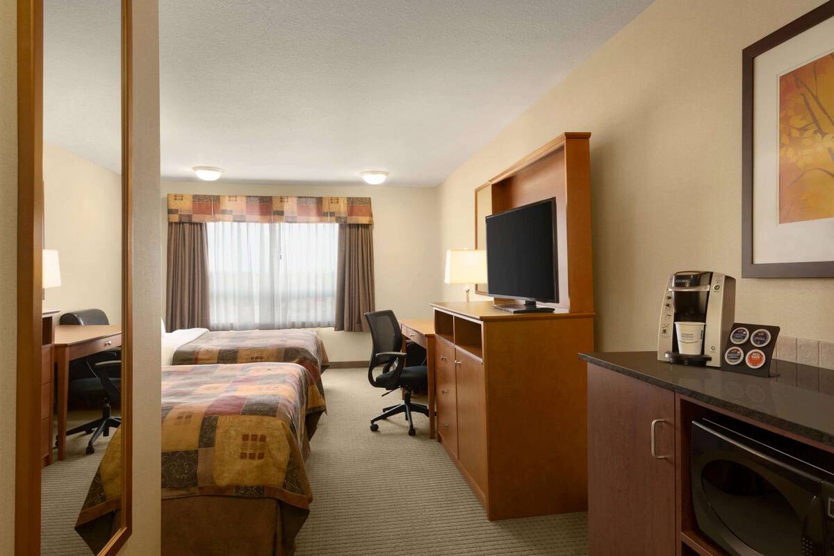 Una habitación de hotel con dos camas, un escritorio con computadora, televisión, microondas y cafetera.
