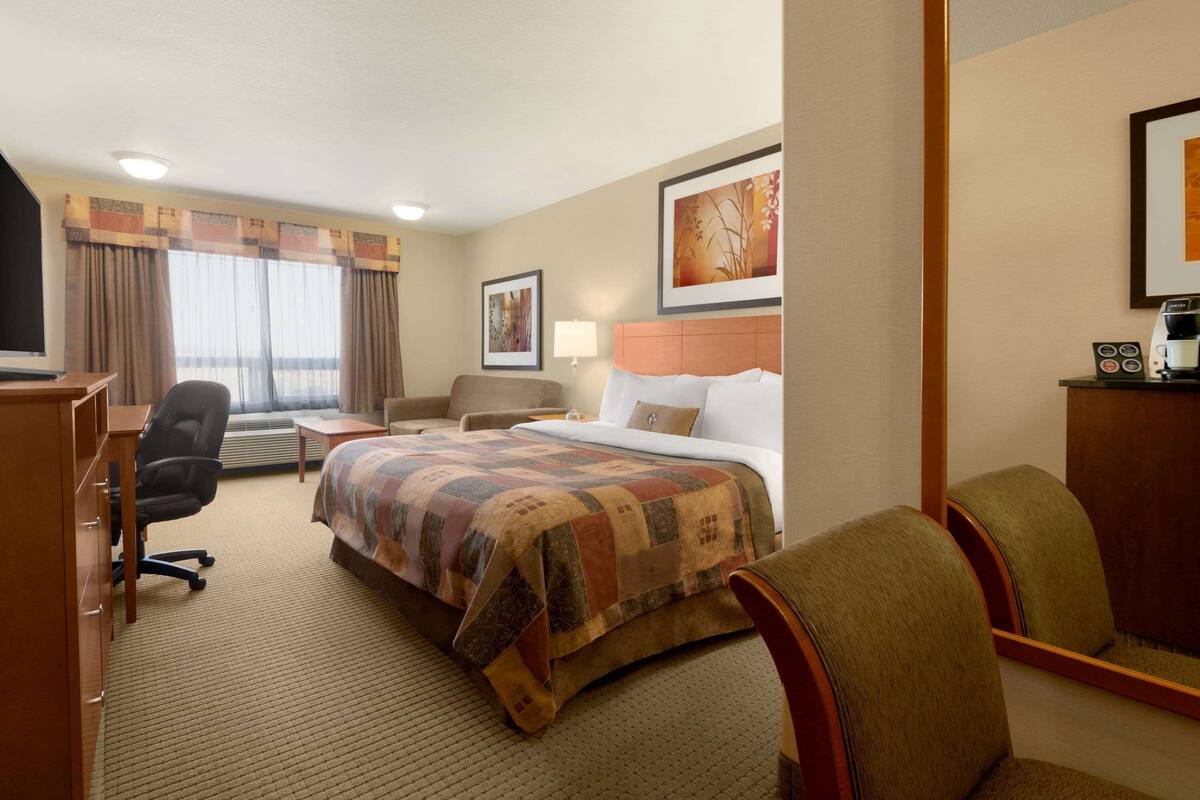 Habitación de hotel con cama, escritorio, silla, lámpara y un cuadro en la pared.