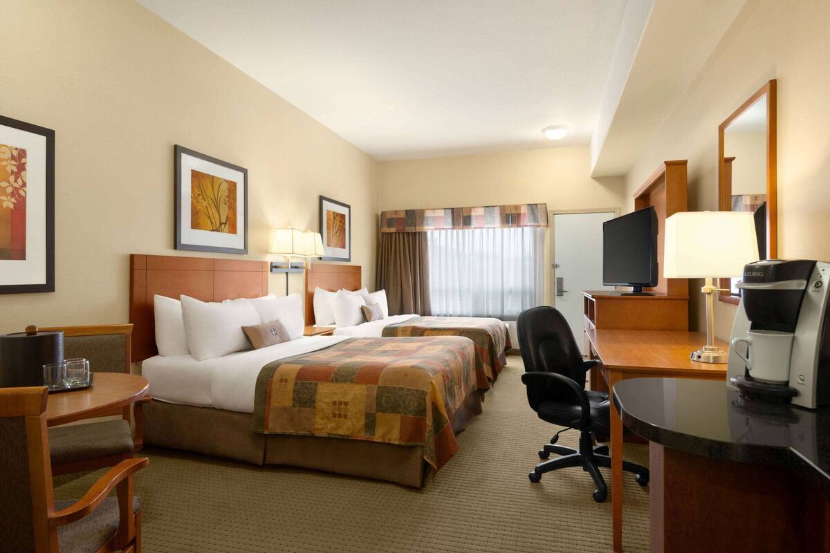 Habitación de hotel con dos camas, un escritorio con computadora, una silla y una cafetera.
