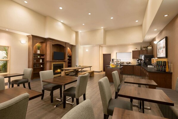 Un amplio comedor con varias mesas y sillas, una chimenea y una zona de cocina con estación de café.