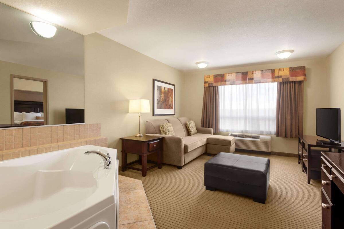 Habitación de hotel con una bañera grande, un sofá, un televisor y una ventana con cortinas.