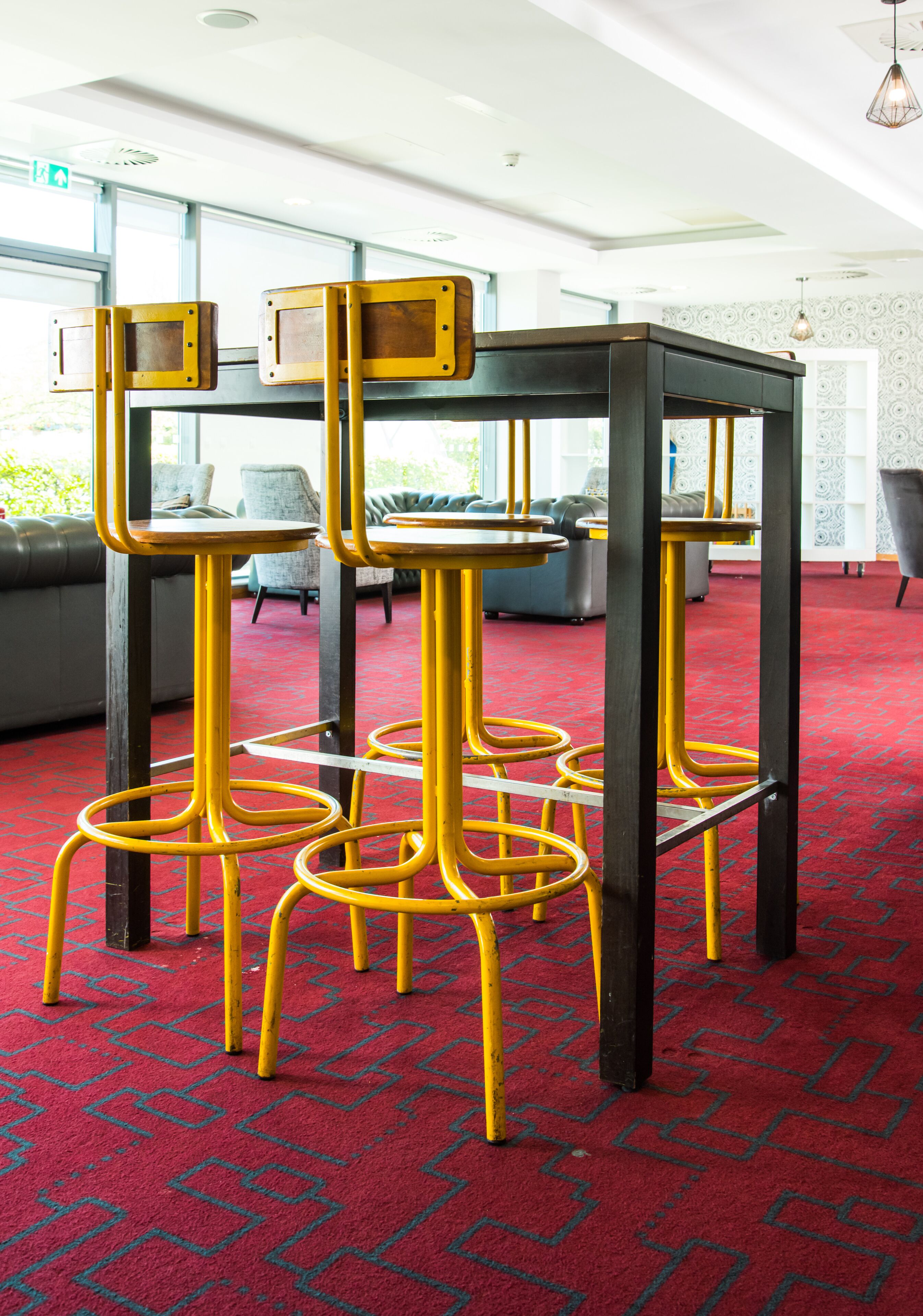 Een modern interieur met een rood tapijt met patroon, een zwarte tafel met gele stoelen en een grijze bank op de achtergrond.