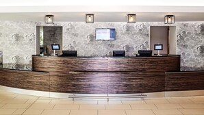 A reception desk with a marble wall backdrop, two monitors, and a wooden counter. - ibis Styles Crewe (Crewe)