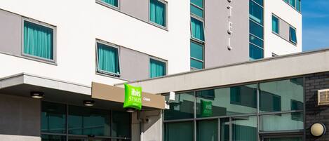 A modern hotel with a flat facade, large windows, and a green sign indicating it is part of the ibis Styles hotel chain.