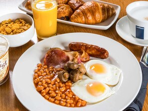 A breakfast plate with eggs, beans, mushrooms, sausages, and a ham steak.