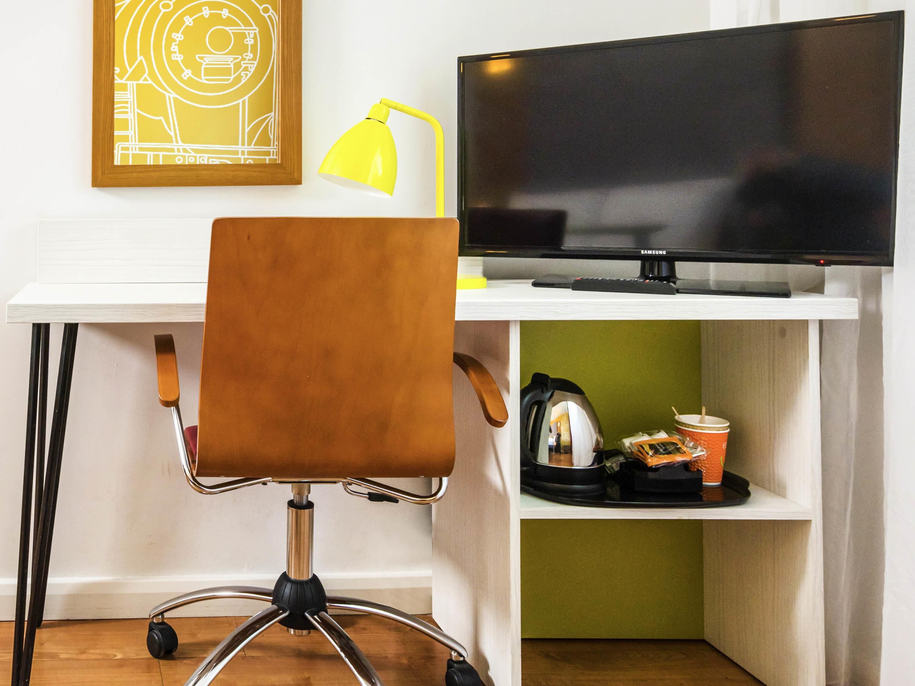 Een werkplek met een bureau, stoel, monitor, lamp en een plank met een koffiekop en waterkoker.