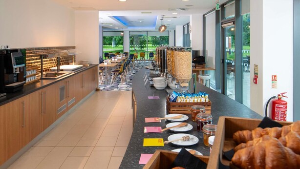 A breakfast buffet area with a variety of food items, including pastries and condiments, and a seating area with tables and chairs. - ibis Styles Crewe (Crewe)