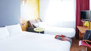 Habitación de hotel con dos camas, un escritorio con silla, televisor y ventana con cortinas.