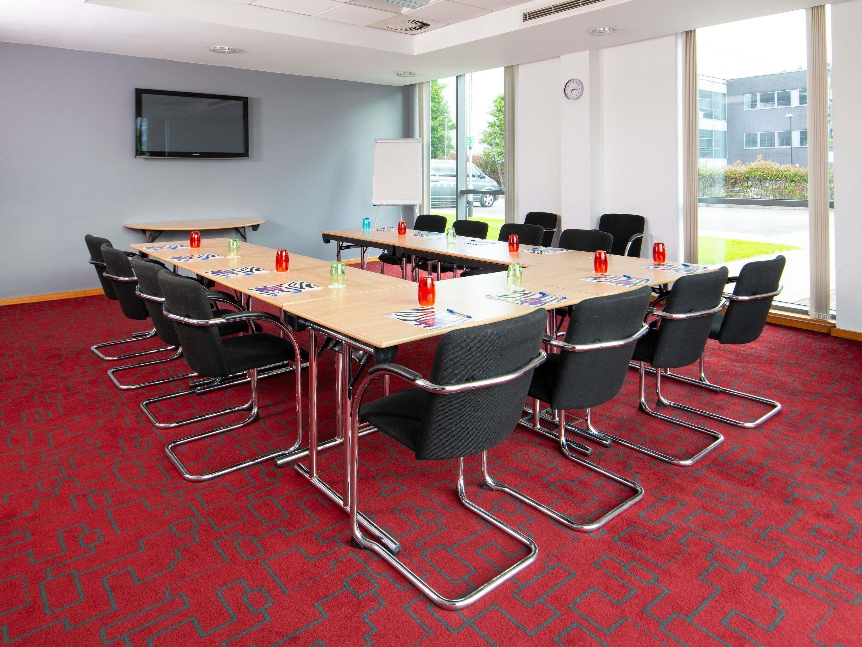 A conference room with a large table, chairs, a whiteboard, and a TV on the wall.