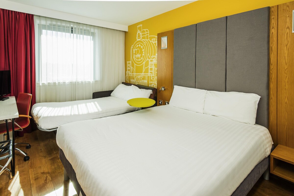 A hotel room with two beds, a desk, a chair, and a window with curtains.