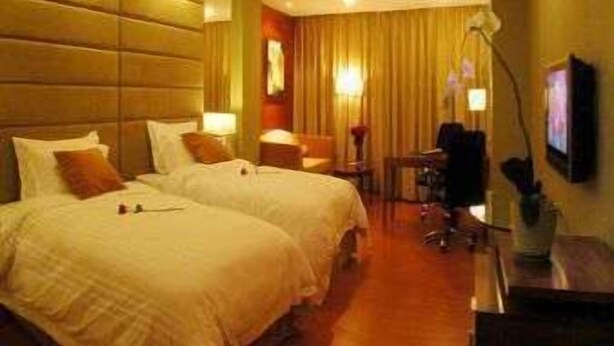 Ein Hotelzimmer mit zwei Betten, einem Schreibtisch, einem Sessel und einem Fernseher.