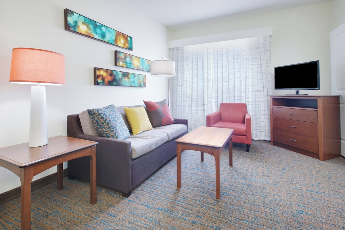 A modern hotel room with a sofa, two armchairs, a TV, and artwork on the wall.
