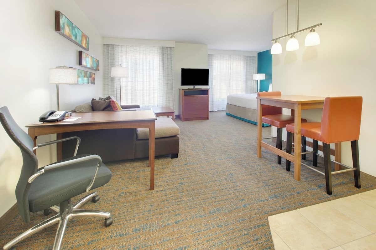 A hotel room with a desk, office chair, sofa, and a dining area with chairs.