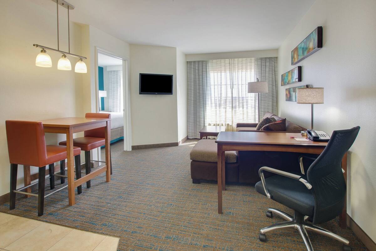 A hotel room with a dining area, a sofa, a desk with a computer, and a TV.