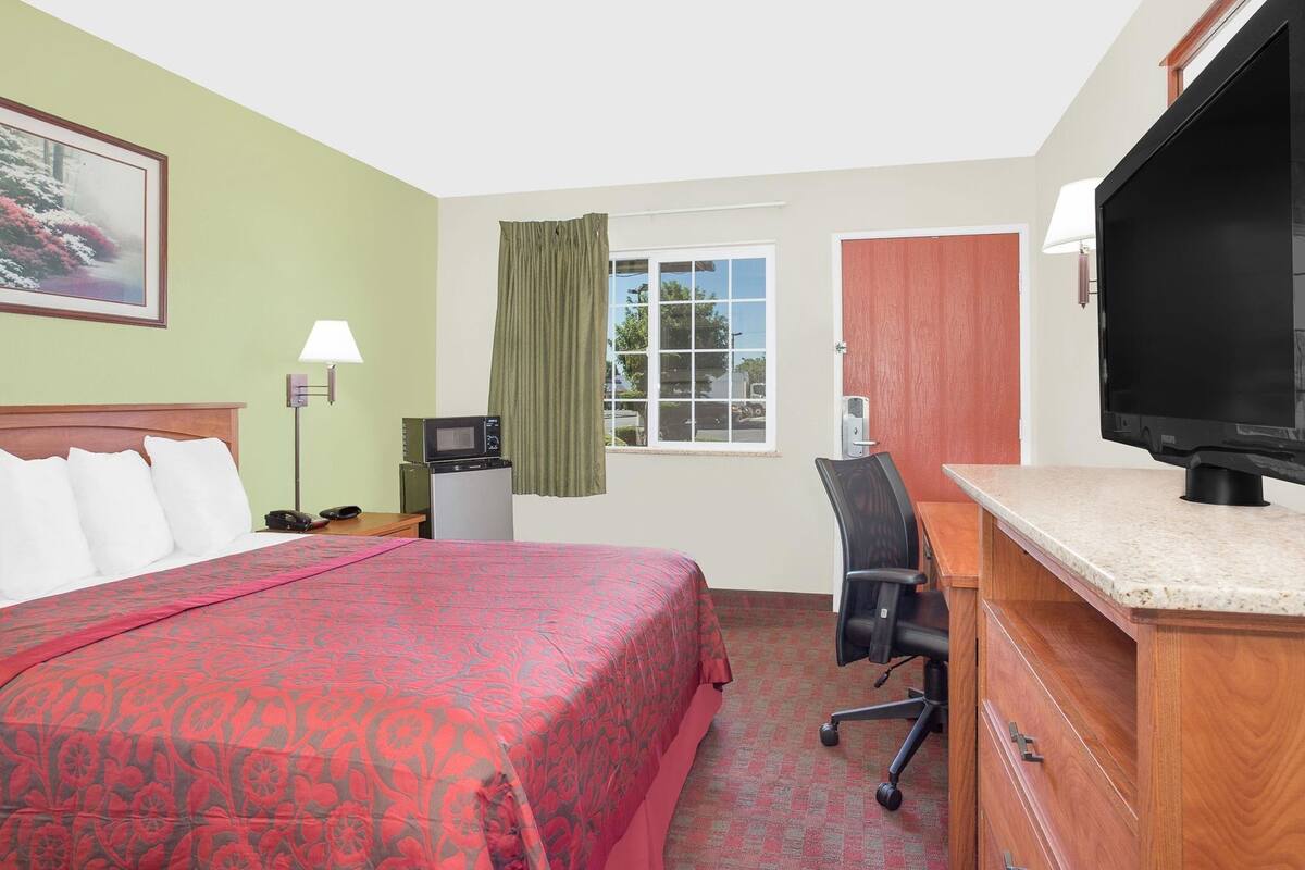 A hotel room with a bed, desk, television, and a window with curtains.