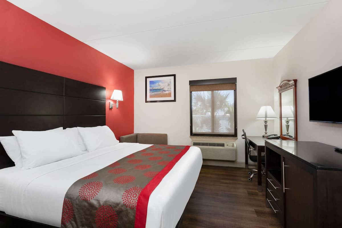 A hotel room with a bed, a desk, a chair, a TV, a window, and a picture on the wall.