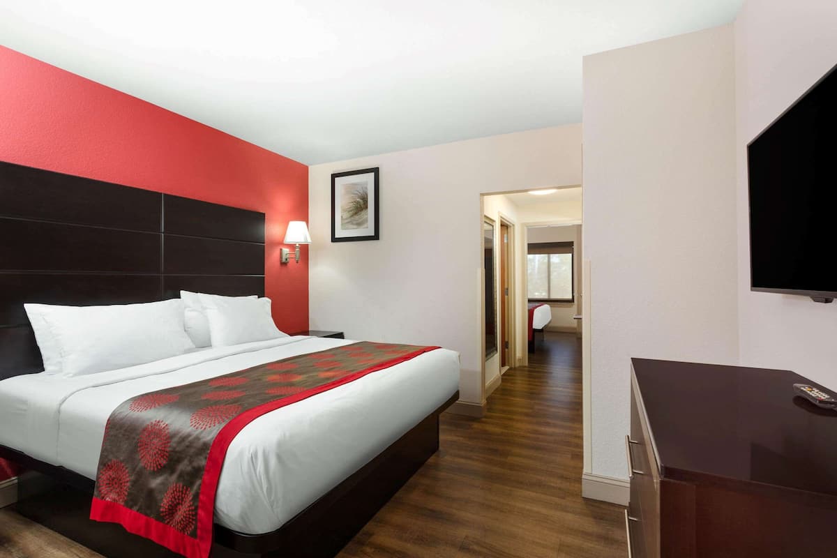 A hotel room with a large bed, a desk, a TV, and a door leading to a bathroom.