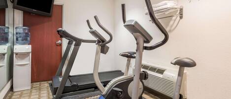 A hotel room with two exercise bikes, a water dispenser, and a television mounted on the wall.