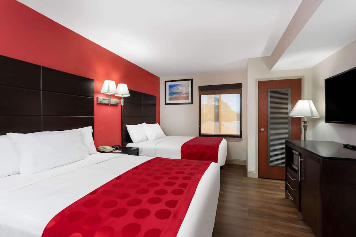 A hotel room with two beds, a TV, a desk, and a window with a view.