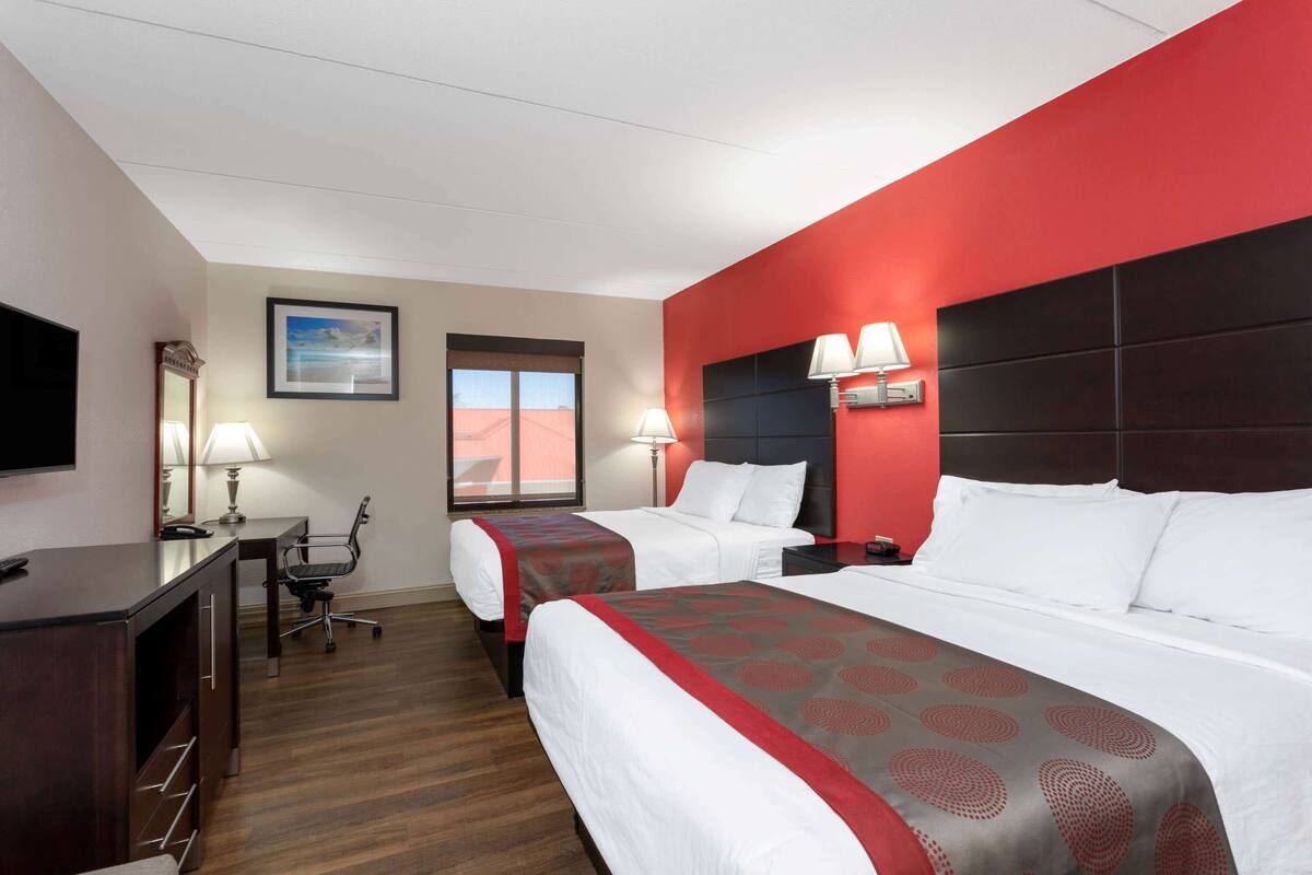 A hotel room with two beds, a desk, a chair, a TV, and a window with a view.