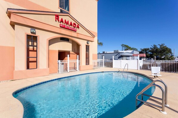 Zona de piscina con un edificio que dice 'RAMADA BY WYNDHAM' al fondo.